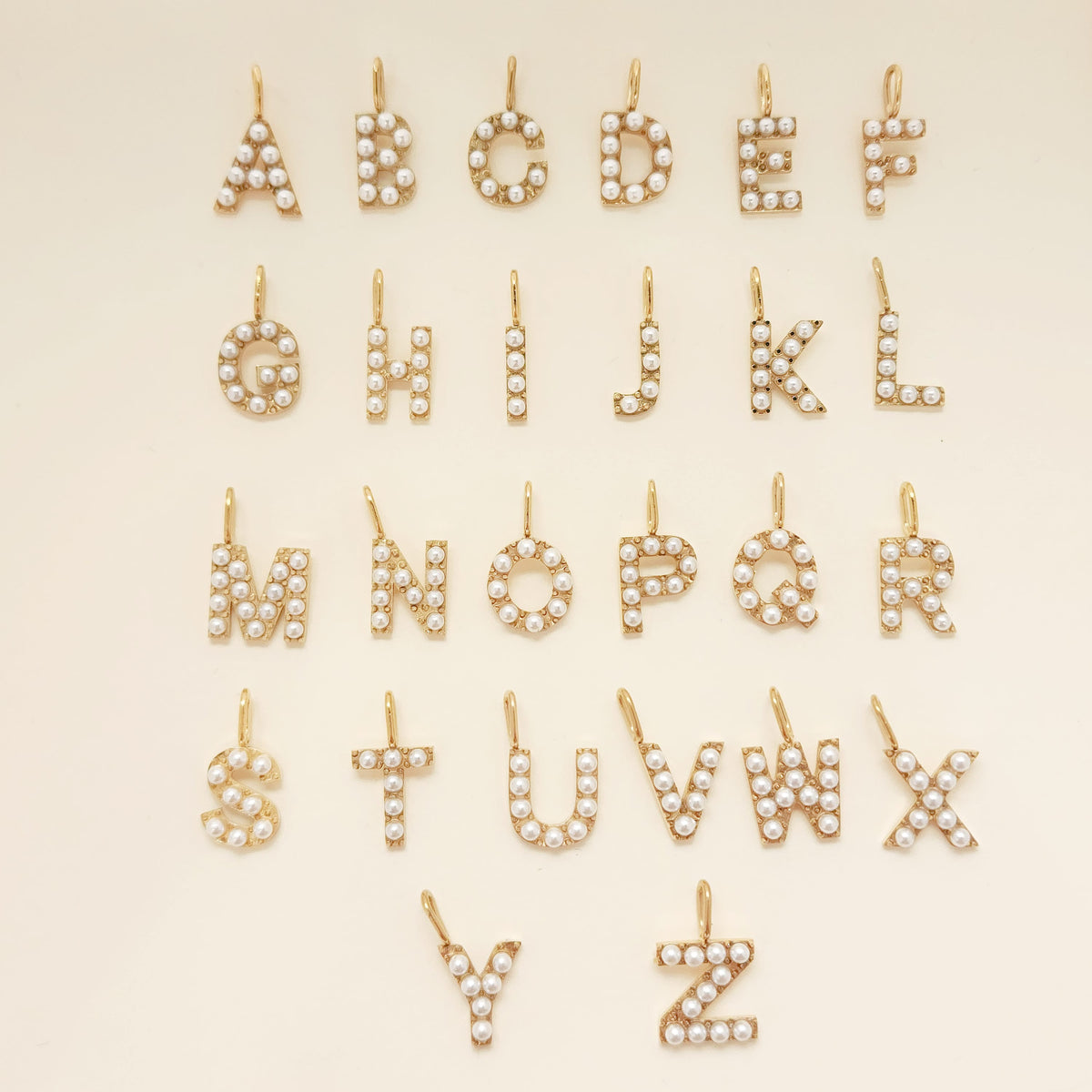 Gold letter pendants with pearls on a beige background