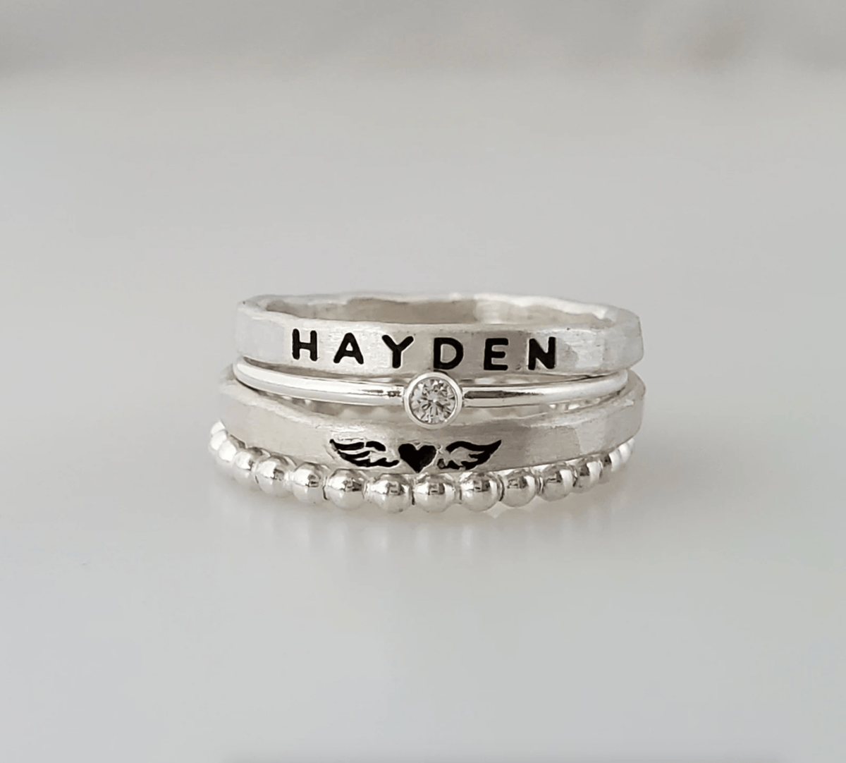 Memorial Ring Set with engraved name ring, angel wing ring, beaded stacking ring, and cubic zirconia ring in sterling silver, fine silver, and 14K gold-filled options.
