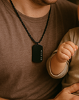 Man wearing a necklace with a dog tag, holding a child's hand.