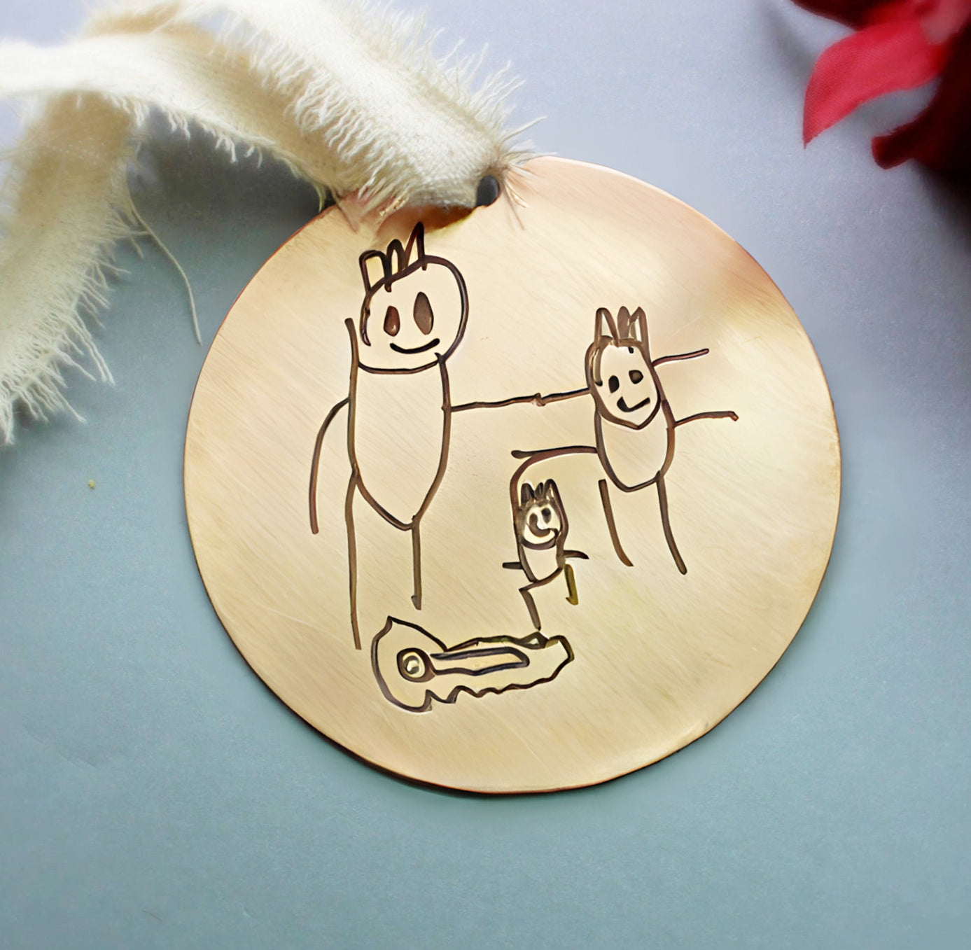 Engraved gold ornament with custom child drawing, cream ribbon and red accents