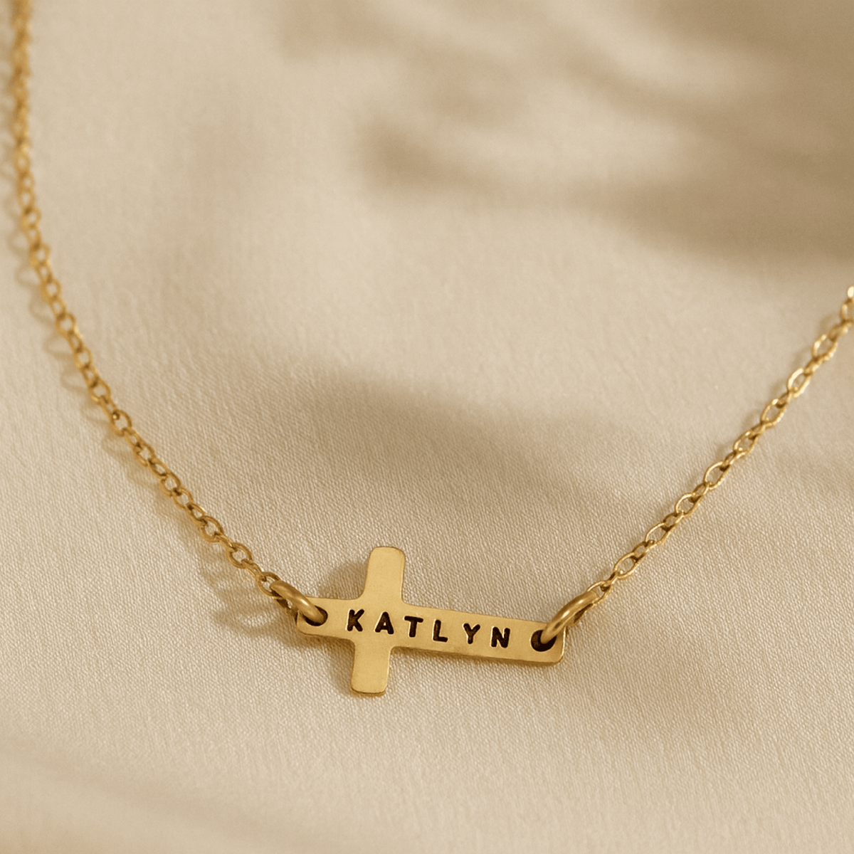 14K gold-filled personalized cross necklace engraved with the name Katlyn on cream background