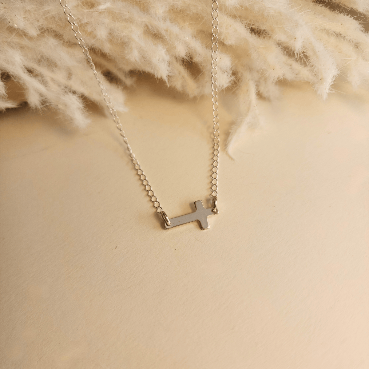 Sterling silver personalized cross necklace with blank engraving displayed on cream knit fabric