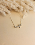 Sterling silver personalized cross necklace with blank engraving displayed on cream knit fabric