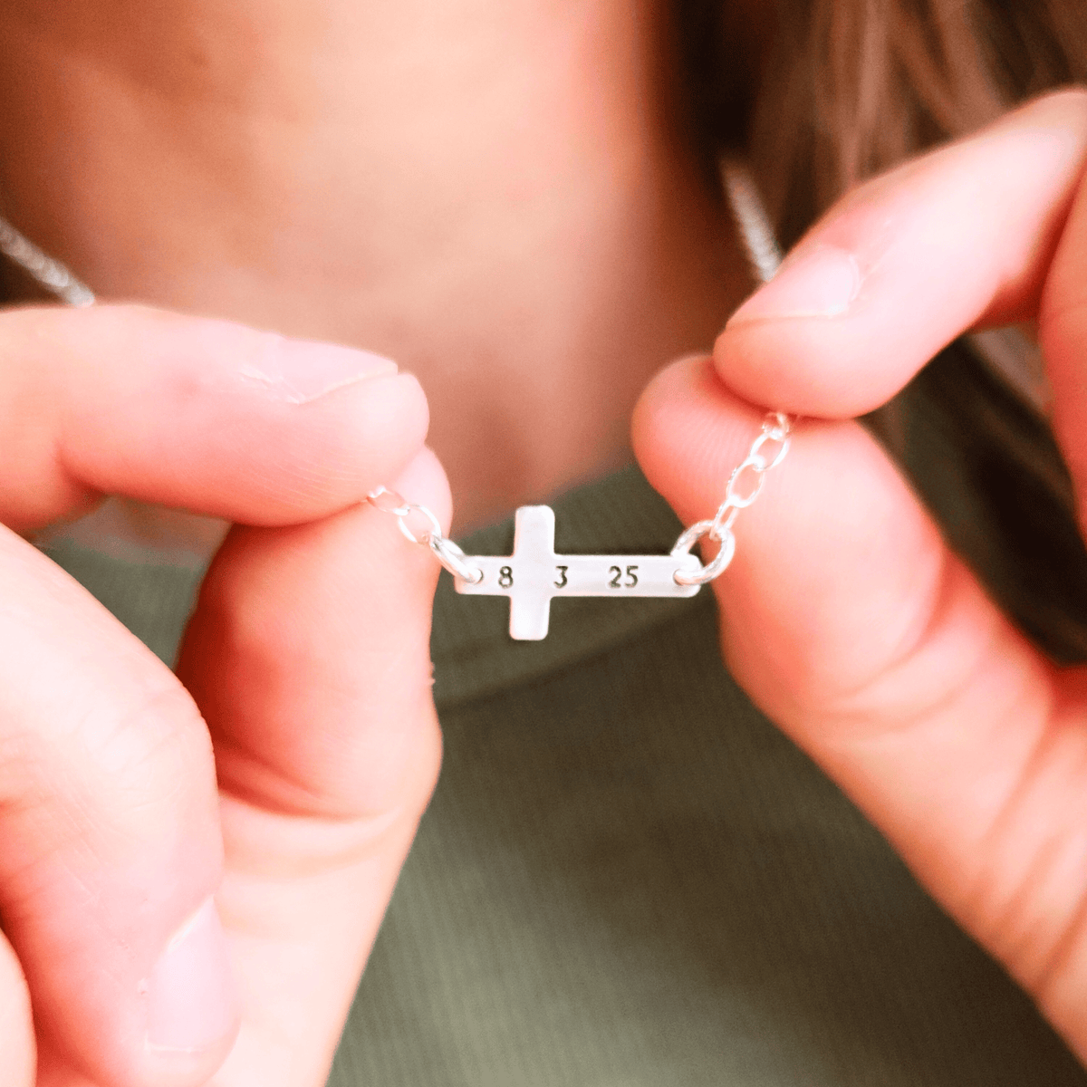 Close-up of sterling silver personalized cross necklace engraved with date 8 3 25 held in hands