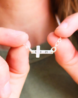 Close-up of sterling silver personalized cross necklace engraved with date 8 3 25 held in hands