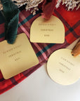 Gold 'First Christmas' tags for Sophia, Dawson, and Liam on a red plaid fabric background.