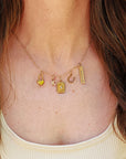 Gold necklace with various charms on a person wearing a beige top.