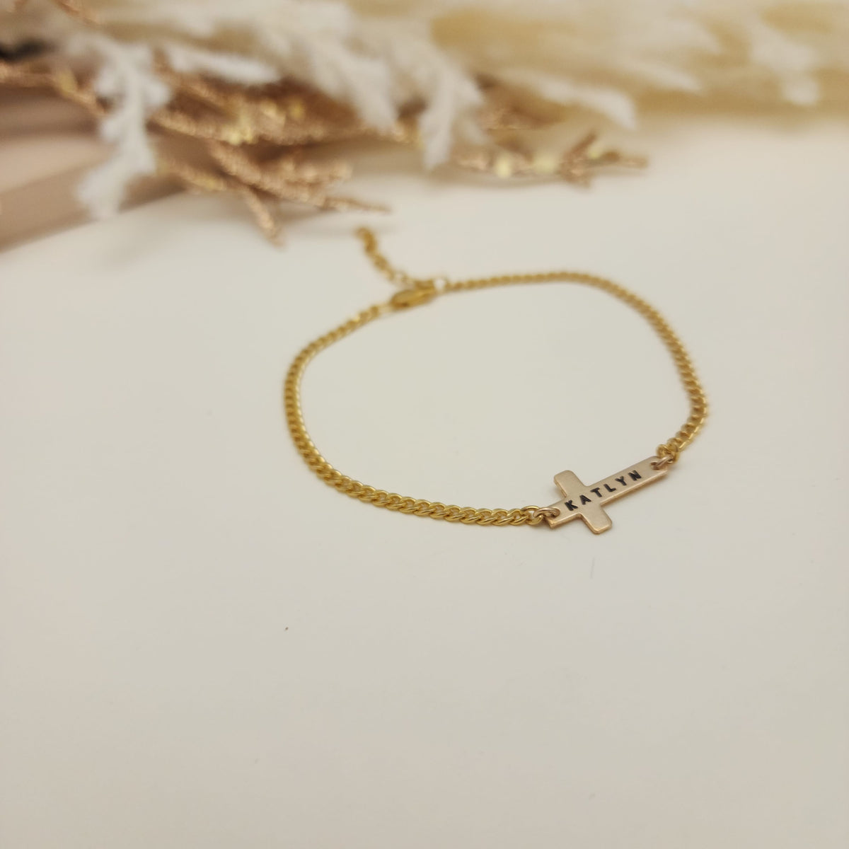 Gold bracelet with a cross charm on a soft beige background