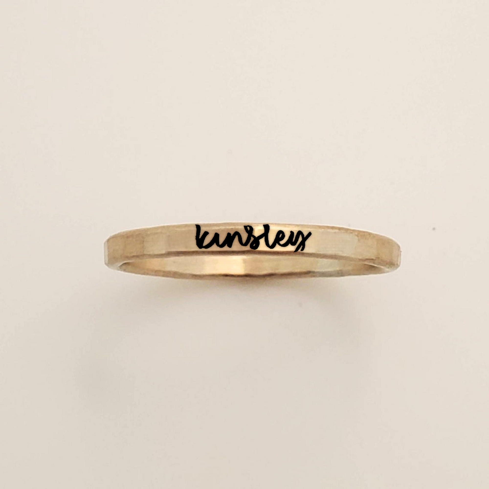 Gold ring with 'kensley' engraved on a beige background
