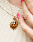 Gold necklace with a pendant held by a hand on a beige fabric background