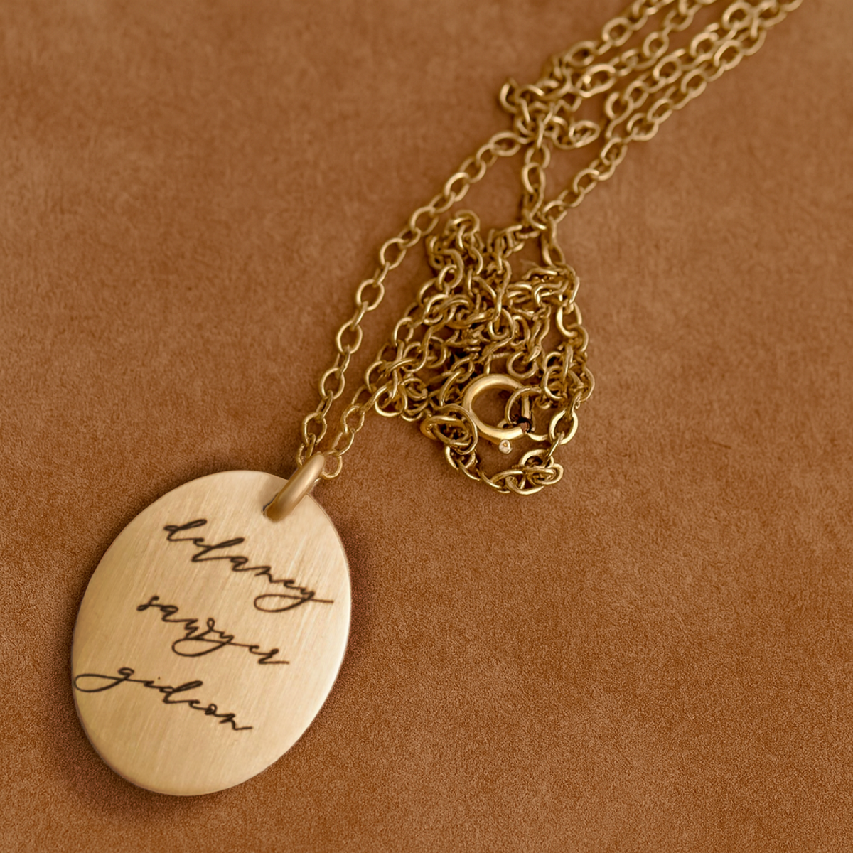 Personalized oval name necklace in sterling silver with hand-stamped cursive names on box chain