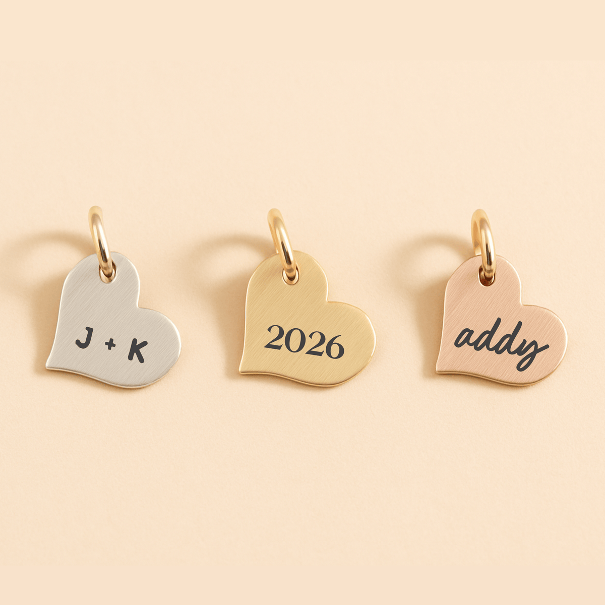 Three heart-shaped gold pendants with engraved text on a beige background