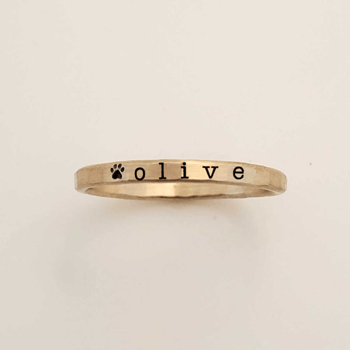 Gold ring with 'olive' and a paw print on a beige background