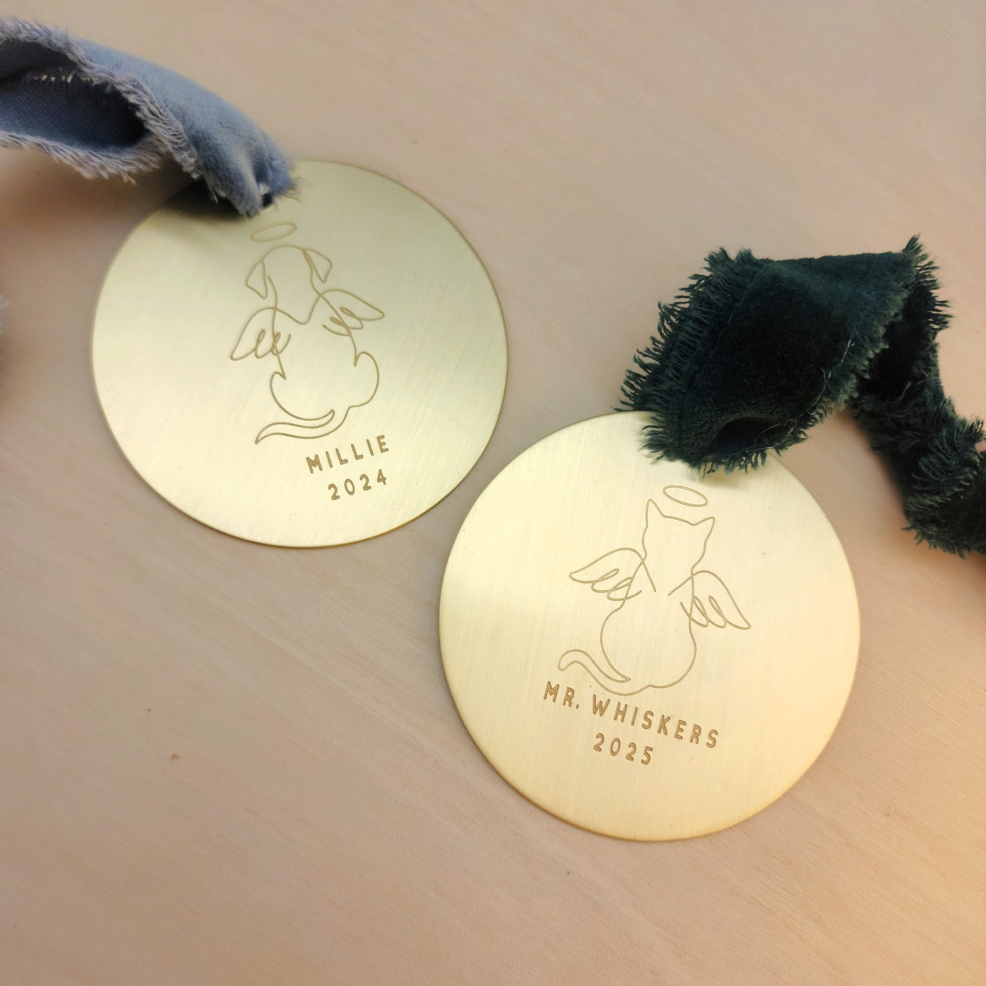 Two gold pet tags with engraved designs and text on a beige surface.