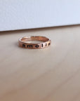 A rose gold filled personalized stacking ring with the name 'amelia' engraved on it, displayed on a wooden surface.