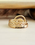 A set of three rings, with the top ring featuring a rainbow design, the middle ring engraved with the name 'Vincent', and the bottom ring with a hammered woven texture. They appear to be made of a gold-filled or sterling silver metal.