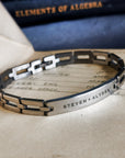 Silver bracelet with engraved names on a surface with an old book in the background