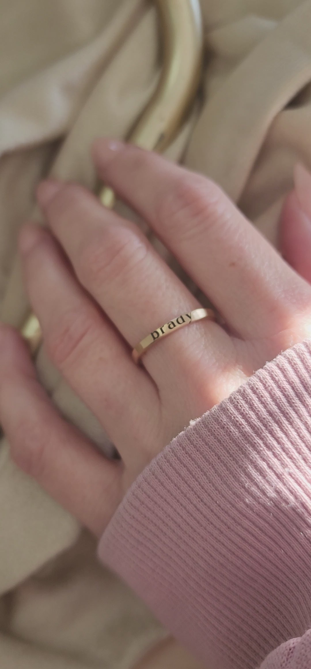 Woman's hand with stacking name ring on the middle finger.  The ring is a 2mm yellow gold ring with a name "brady" engraved in dark letters.