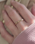 Woman's hand with stacking name ring on the middle finger. The ring is a 2mm yellow gold ring with a name "brady" engraved in dark letters.