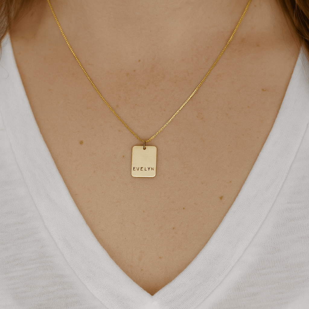 Gold necklace with a tag worn by a person on a white background