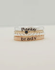 A set of four stackable rings, with the top ring displaying the word 'brady' and a small heart pattern, and a band ring with 'brady' written on it.
