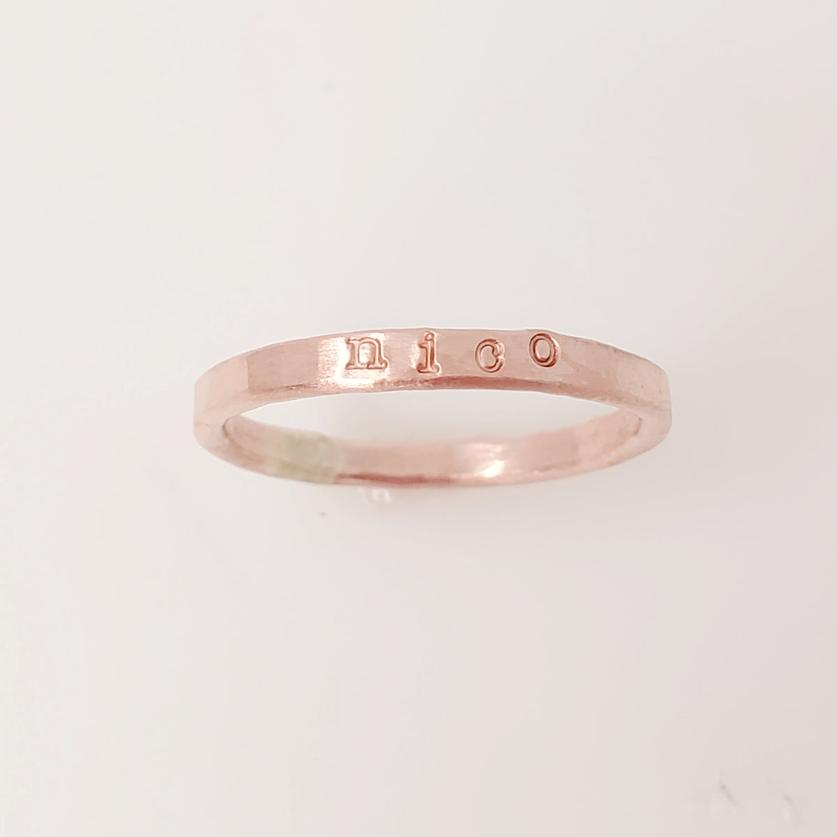 A rose gold-colored stacking name ring with the name 'nico' hand-stamped on it.