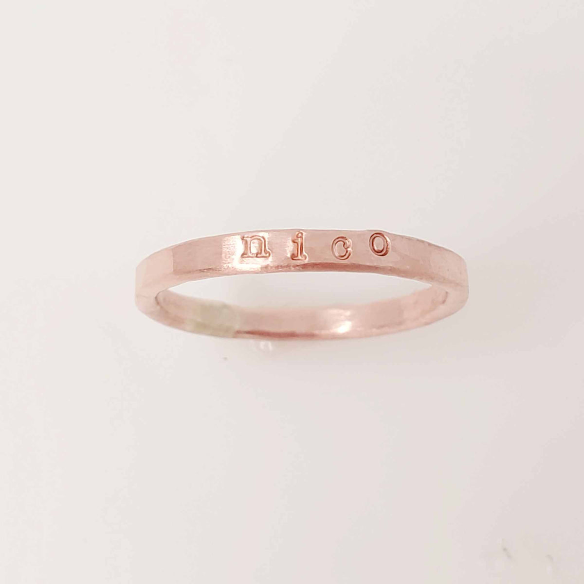 A rose gold-colored stacking name ring with the name 'nico' hand-stamped on it.