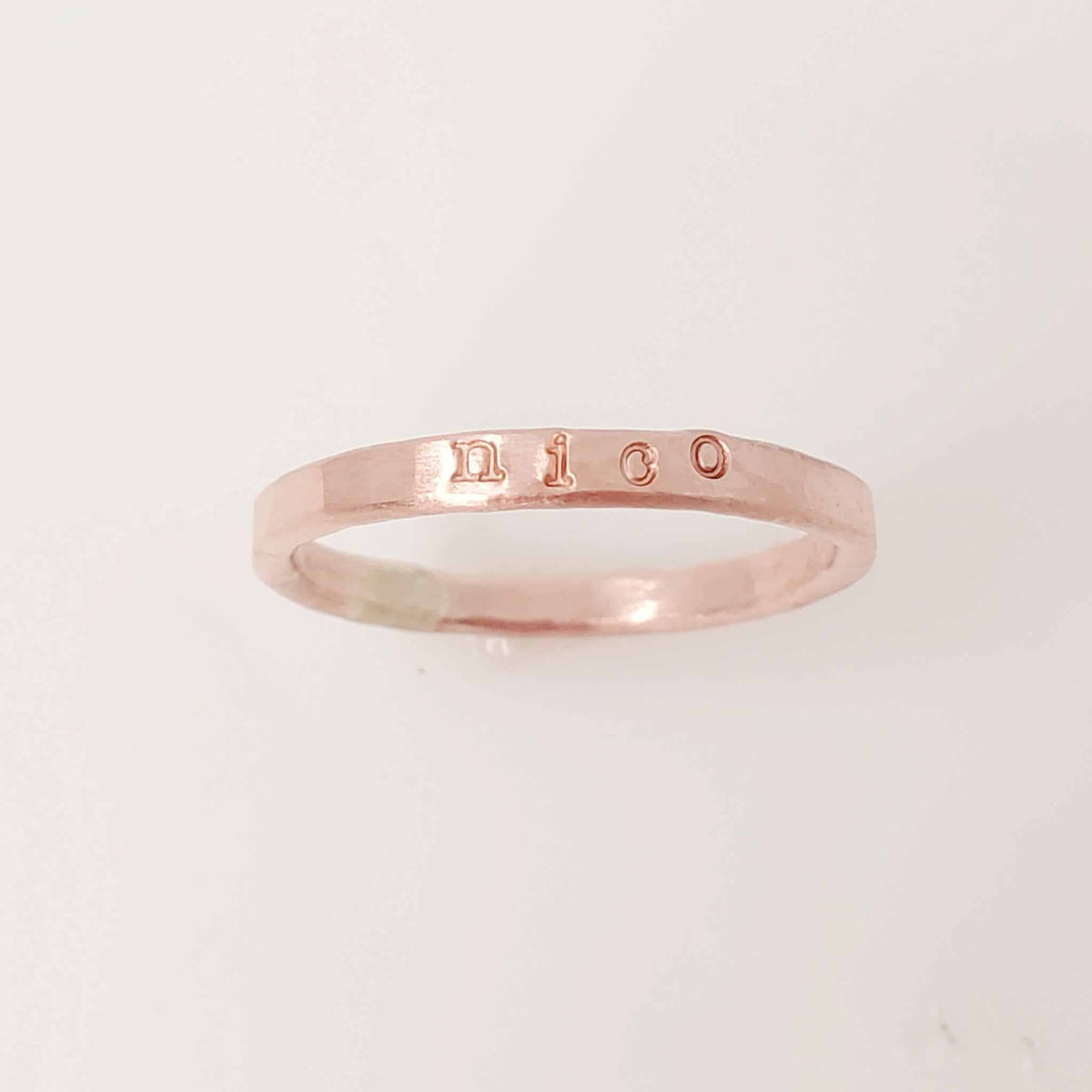 A rose gold-colored stacking name ring with the name 'nico' hand-stamped on it.