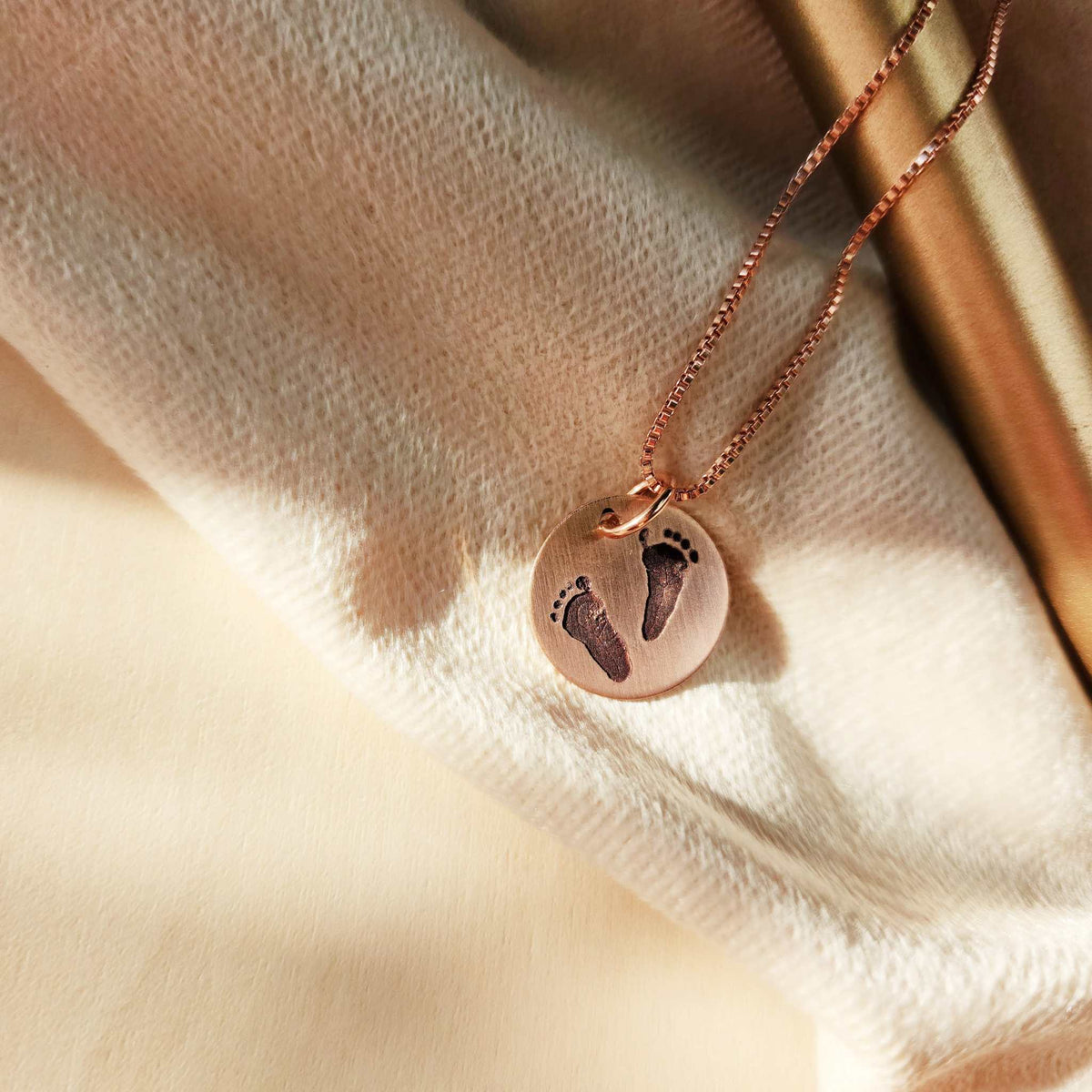 Rose gold necklace with footprints on a soft fabric background