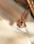 Rose gold necklace with footprints on a soft fabric background