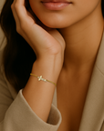 Close-up of a woman's hand wearing a gold bracelet with a cross charm, against a neutral background.