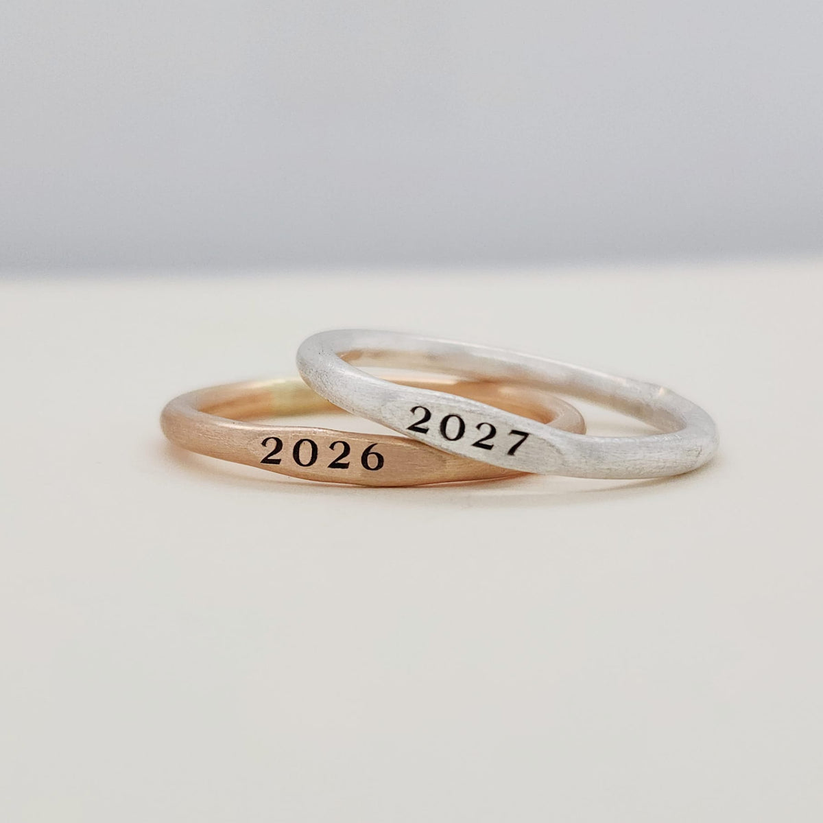Two signet year stacking rings, one with '2026' and the other with '2027', displayed on a white surface.