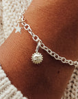 A woman's wrist wearing a silver charm bracelet with a star-shaped charm and a small sun charm attached to it.