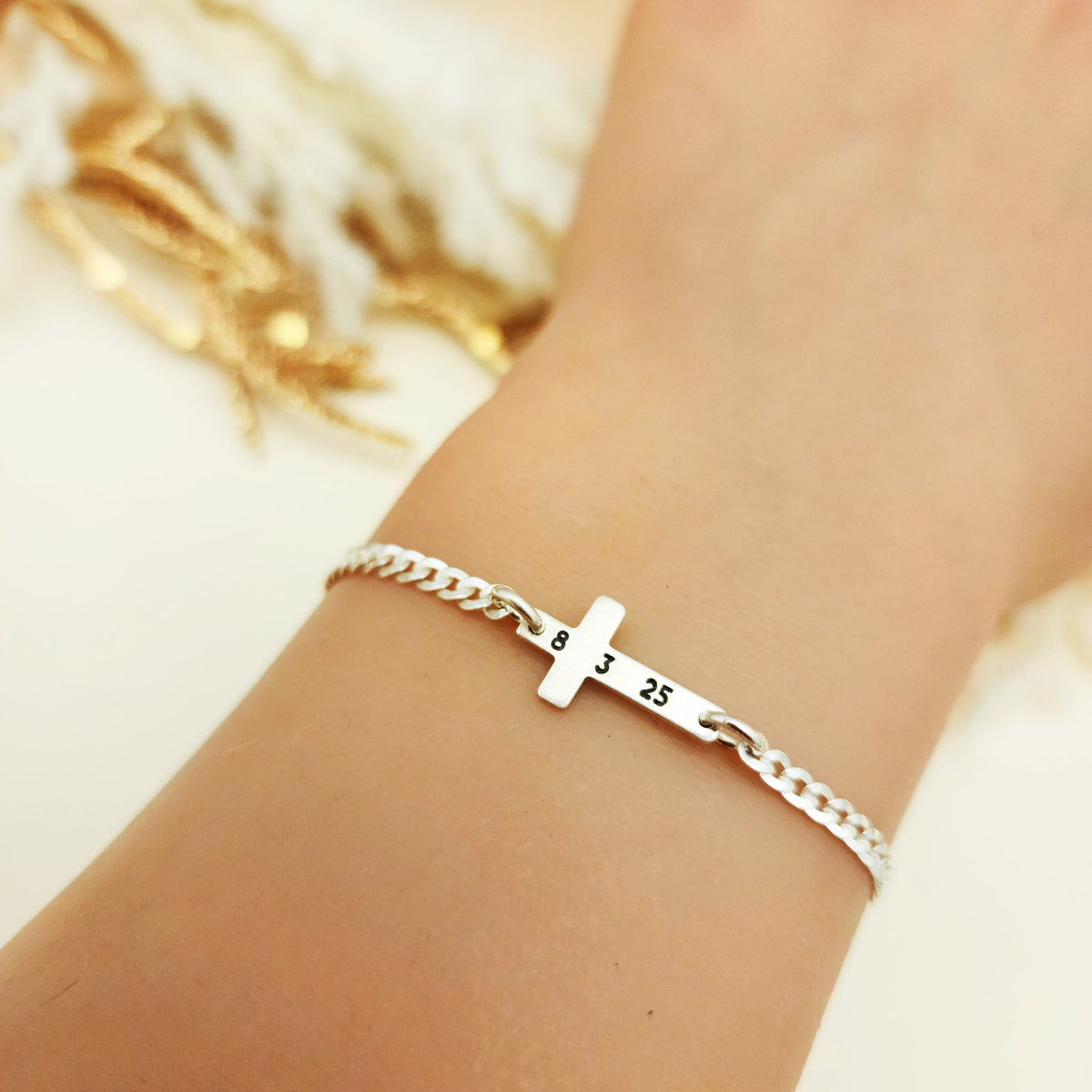 Silver bracelet with a cross charm on a wrist against a neutral background