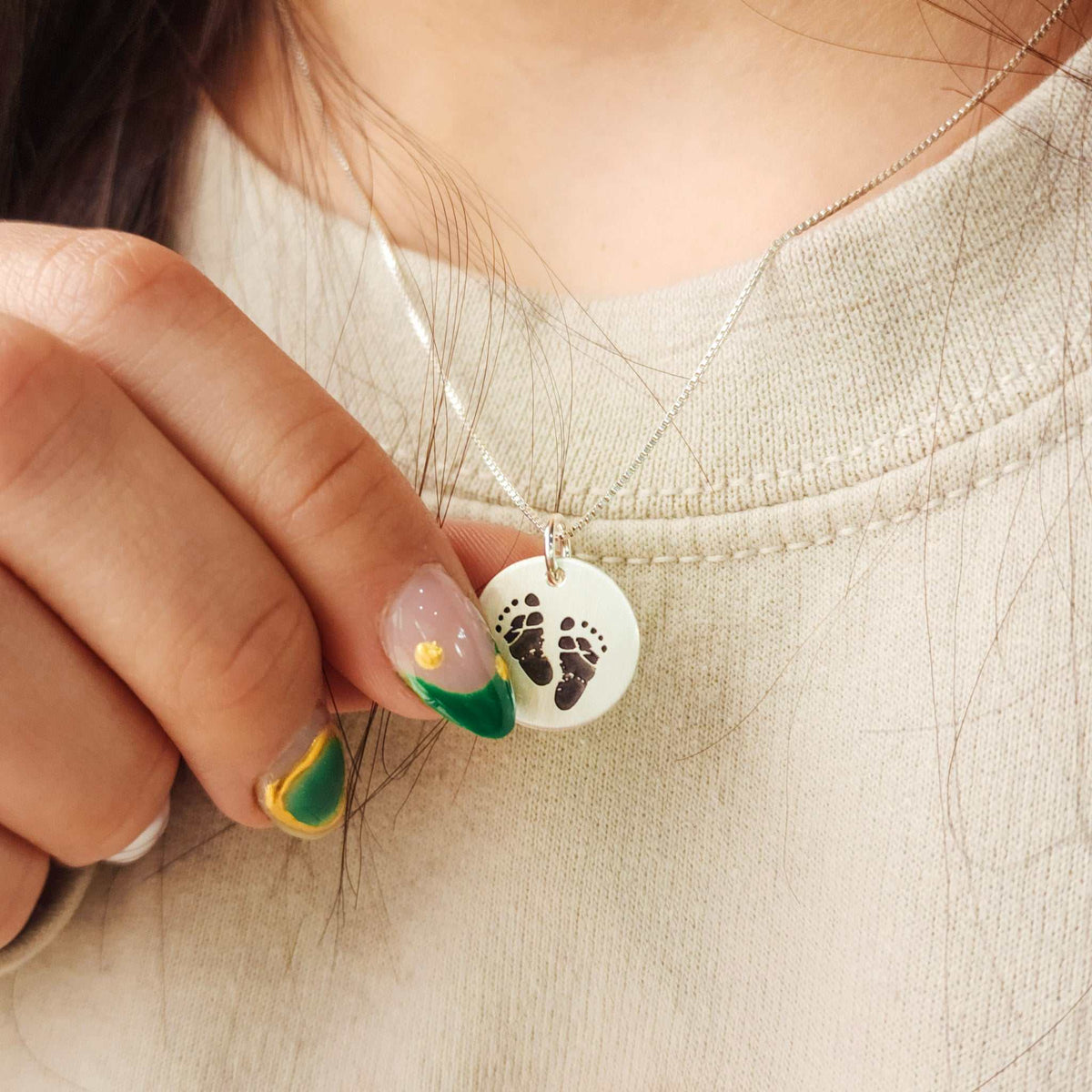 Close-up of a necklace with a pendant featuring footprints held by a hand.