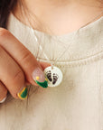 Close-up of a necklace with a pendant featuring footprints held by a hand.