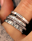 A set of silver stacking name rings with personalized engravings on each ring, displayed on a person's hand.