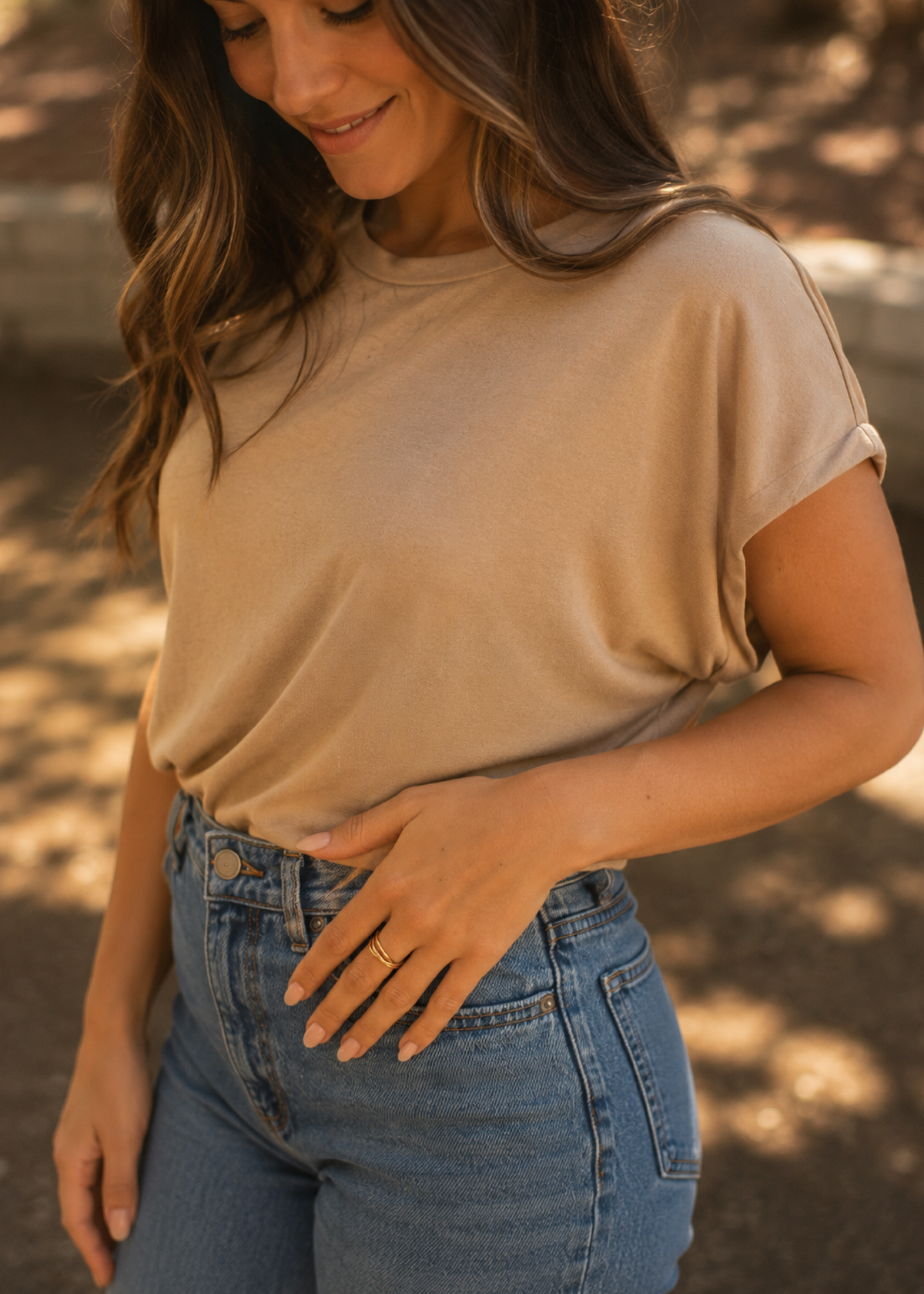 Woman wearing a beige t-shirt and blue jeans with a blurred outdoor background