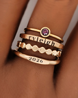 A set of stackable gold rings on a person's hand, featuring personalized engravings such as a name and the year 2026.