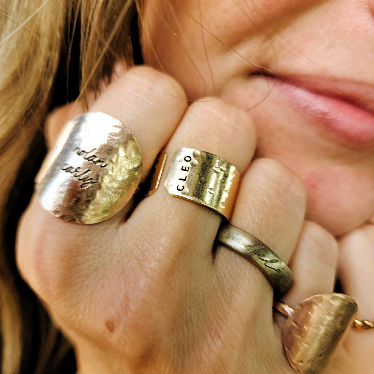 Close-up of a hand wearing multiple gold rings with visible branding.