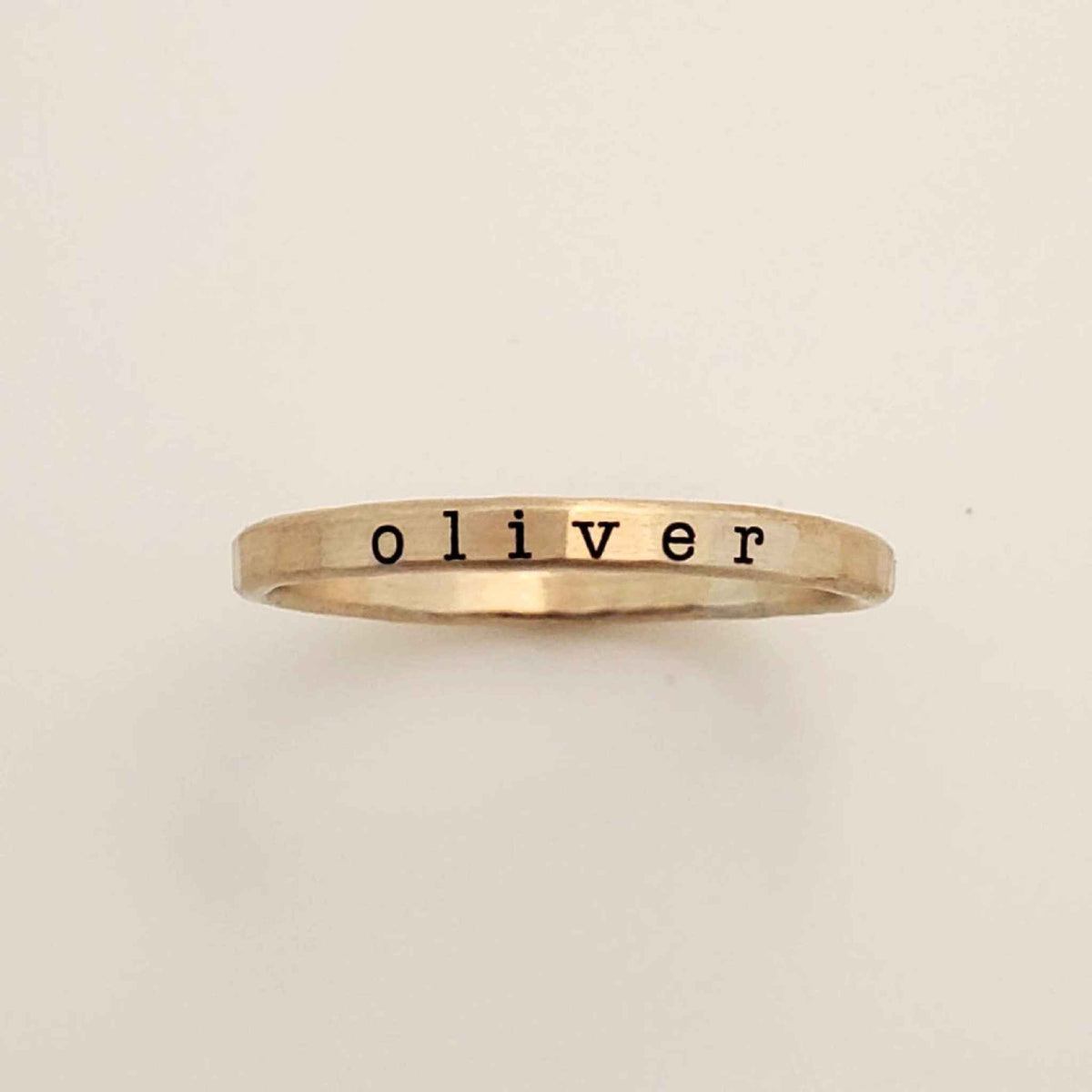 A gold-colored ring with the name 'oliver' engraved in a typewriter-style font.