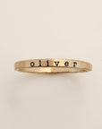 A gold-colored ring with the name 'oliver' engraved in a typewriter-style font.