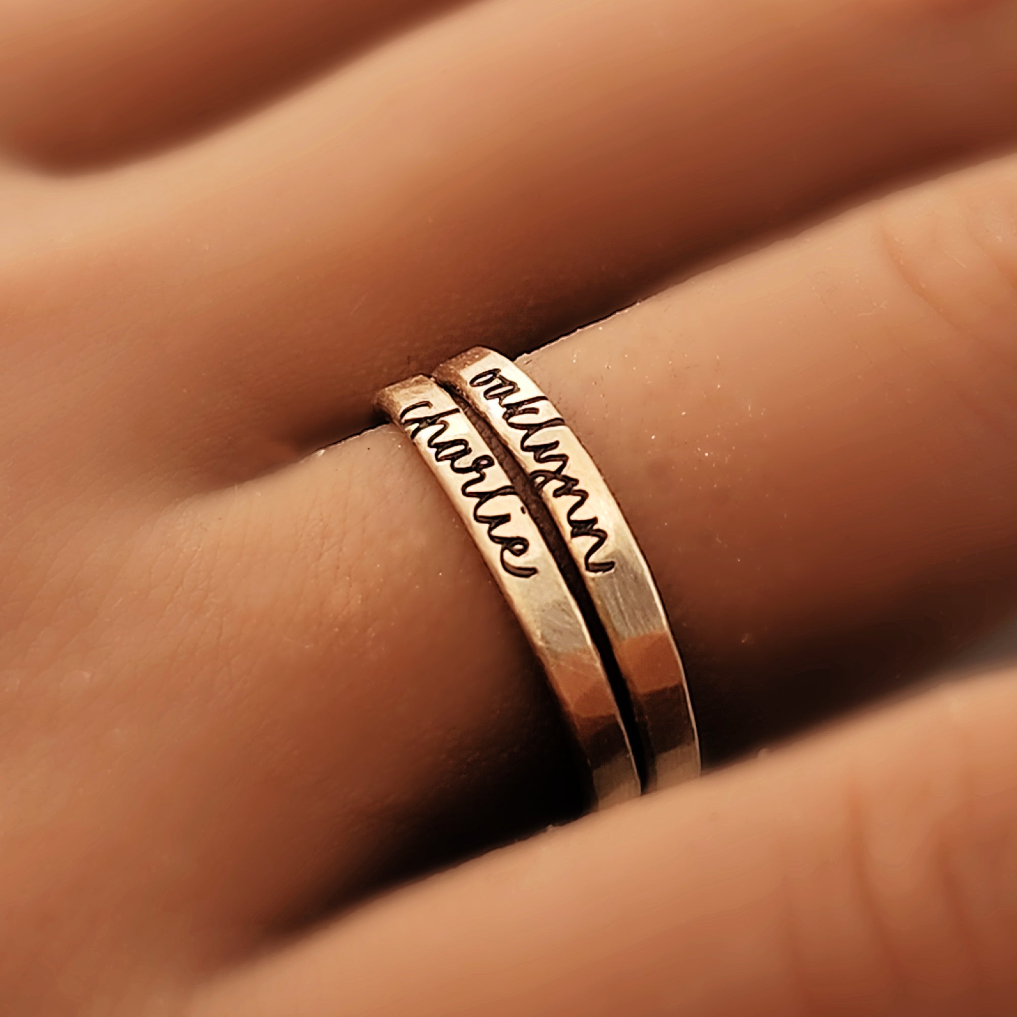 Two gold rings with engraved text on a finger
