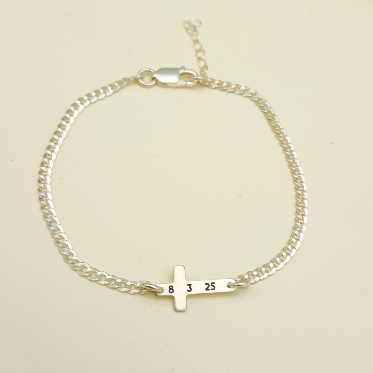 Gold bracelet with a small cross charm on a beige background