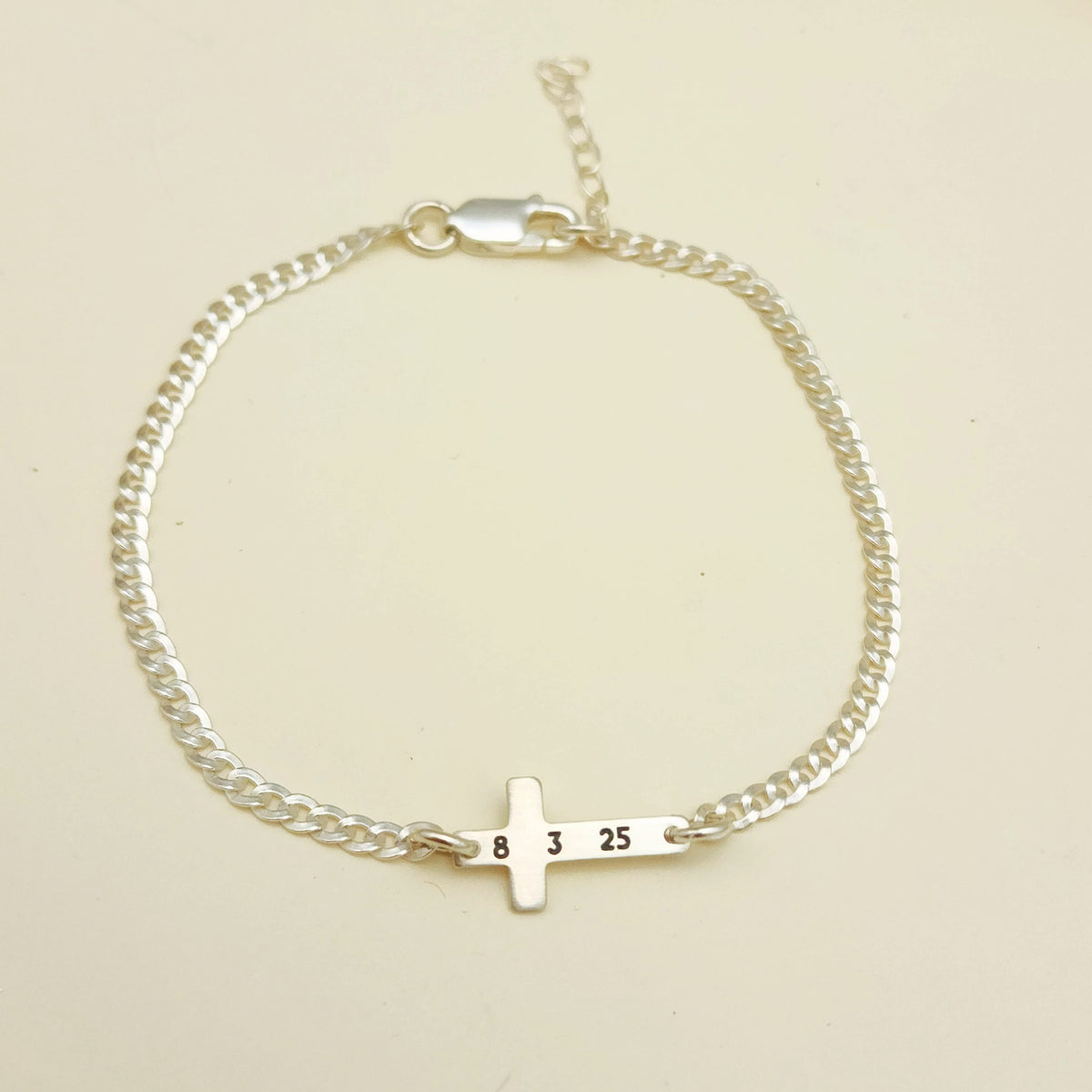 Gold bracelet with a small cross charm on a beige background