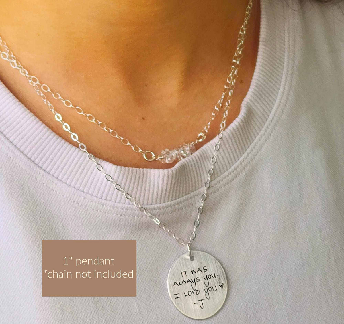 Silver necklace with a pendant worn by a person, on a plain background