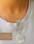 Silver necklace with a pendant worn by a person, on a plain background