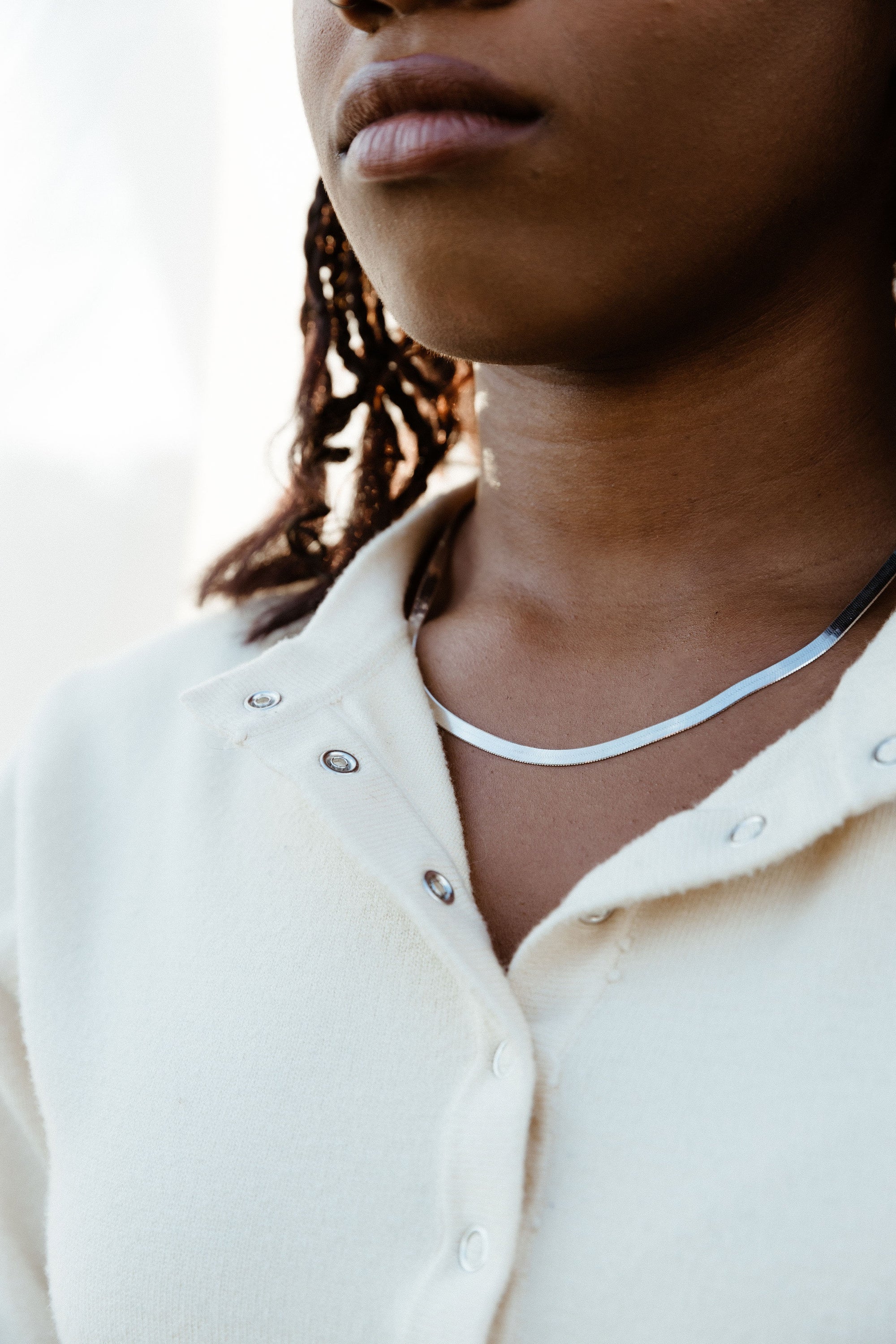 A close-up image of a person wearing a sterling silver herringbone chain necklace with a lobster claw clasp.