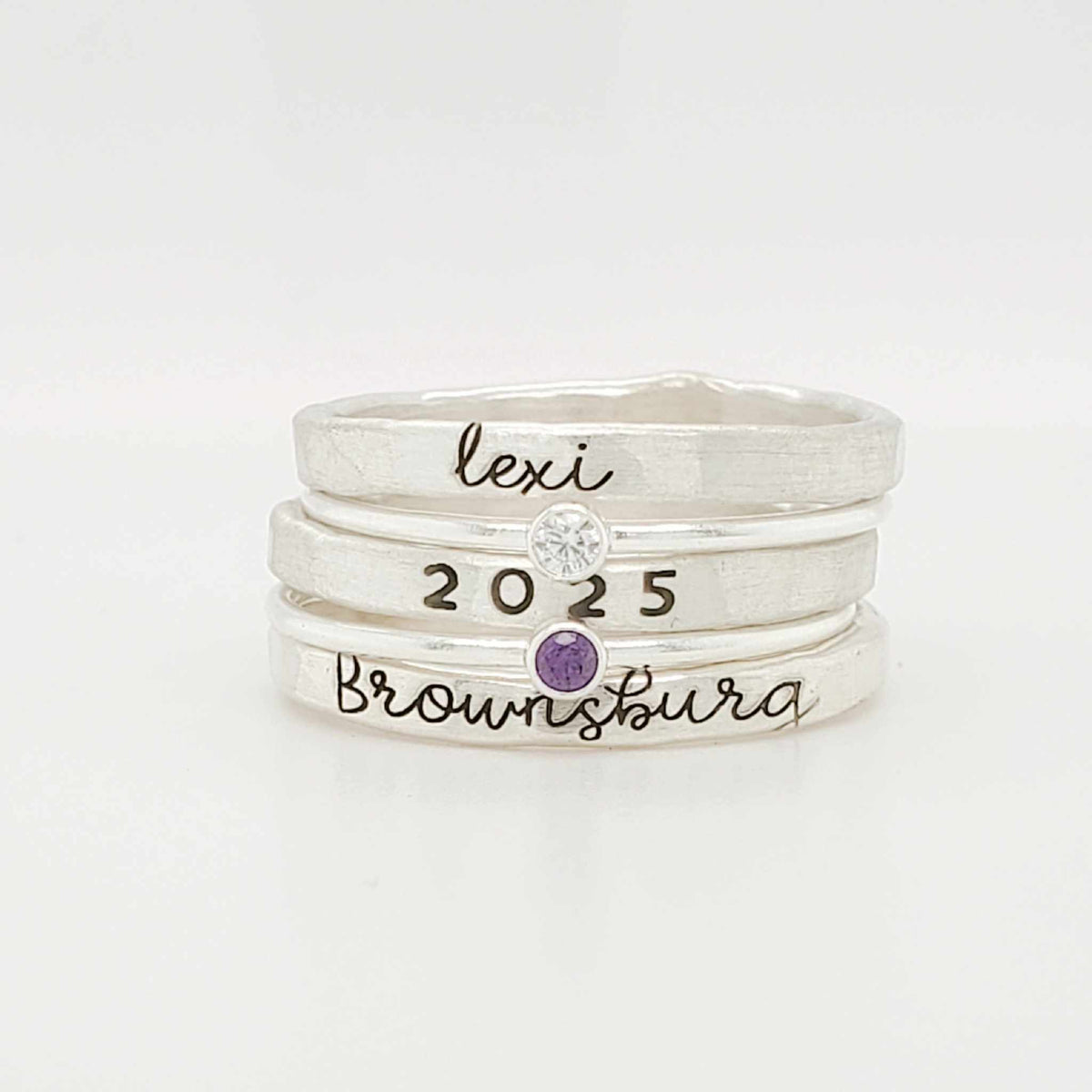 A set of three stackable rings made of yellow gold, with two gemstones, and personalized engravings including 'BROWNSBURG', 'class of 2025' and 'MAREN'.