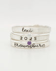 A set of three stackable rings made of yellow gold, with two gemstones, and personalized engravings including 'BROWNSBURG', 'class of 2025' and 'MAREN'.